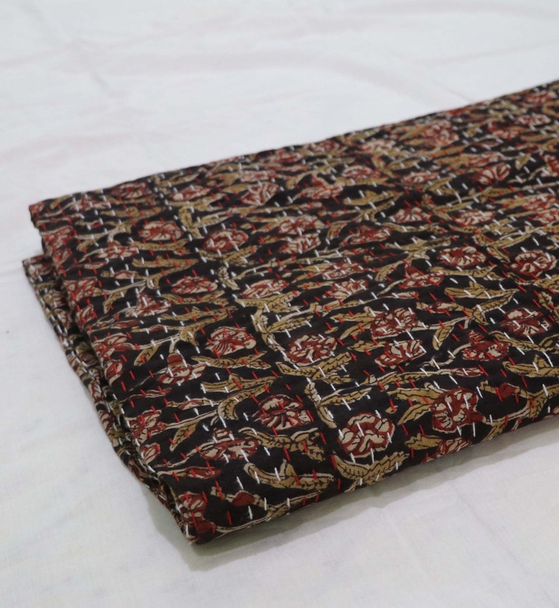 May include: Black cotton fabric with a floral pattern in shades of brown, red, and white. The fabric is quilted with a running stitch in white thread.