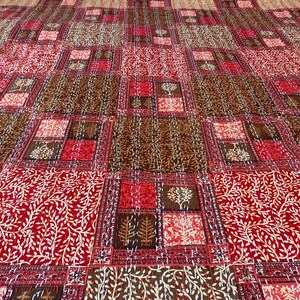 May include: A large, rectangular quilt with a repeating pattern of squares and rectangles in shades of red, brown, and cream. The design includes tree and leaf motifs, creating a warm and inviting textile.