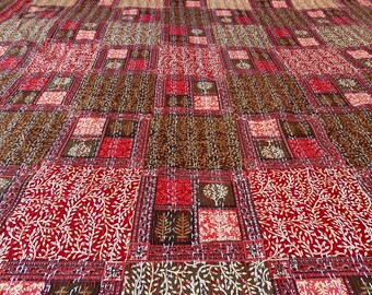 Puede incluir: Un edredón rectangular grande con un patrón repetitivo de cuadrados y rectángulos en tonos de rojo, marrón y crema. El diseño incluye motivos de árboles y hojas.