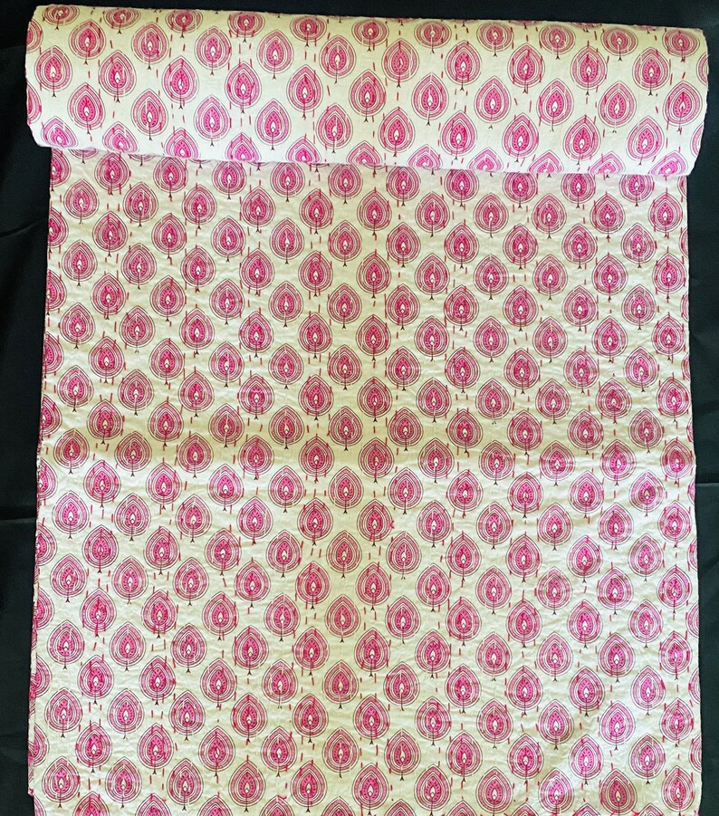May include: A rolled-up fabric with a repeating pattern of pink leaf-like shapes on a cream background. The leaves are outlined with a darker pink stitch, creating a textured effect. The fabric is likely cotton or a similar material.