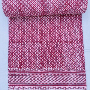 Puede incluir: Una colcha de algodón roja y blanca con un patrón floral. La colcha está doblada por la mitad y la tela es suave y texturizada.