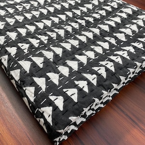 May include: A folded textile featuring a repeating pattern of white triangular shapes on a black background. The fabric displays visible horizontal rows of white running stitches, creating a quilted texture across the entire surface of the material.