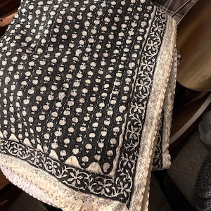 Könnte beinhalten: Ein schwarz-cremefarbenes gestepptes Textil mit einem sich wiederholenden Blumenmuster auf dem Mittelteil. Der Stoff ist mit einer breiten, komplizierten Ranken- und Blattverzierung in Schwarz auf cremefarbenem Grund eingefasst.