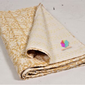 May include: A folded, reversible quilt featuring a floral design in yellow and white. The reverse side is a cream colour with yellow stitching. The quilt is made of soft fabric, suitable for a bed or sofa.