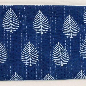 May include: An indigo blue quilt with a repeating pattern of white leaf shapes. The leaves are evenly spaced across the surface. White stitching lines run vertically and horizontally, creating a grid-like texture.