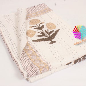 May include: Cream-colored floral quilt with brown and tan accents. The quilt features a large floral design and a decorative border. The stitching is visible throughout the quilt, adding texture and detail. The quilt is folded, showcasing its design.