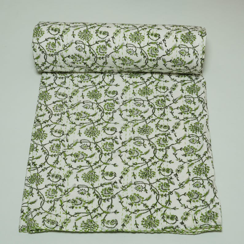 Green floral block print Kantha quilt rolled and unrolled on a white background, soft cotton hand-stitched blanket.