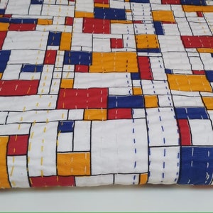 Puede incluir: Un edredón blanco con un diseño geométrico que presenta bloques rojos, azules y amarillos. El edredón está cosido a mano con hilo blanco, creando un patrón similar a una cuadrícula. La estética general es moderna y colorida, adecuada para una cama o como manta decorativa.