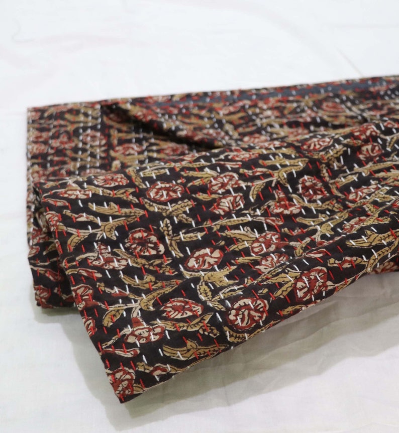 May include: A black cotton kantha quilt with a floral pattern in shades of brown, red, and white. The quilt is folded in half and has a hand-stitched design.