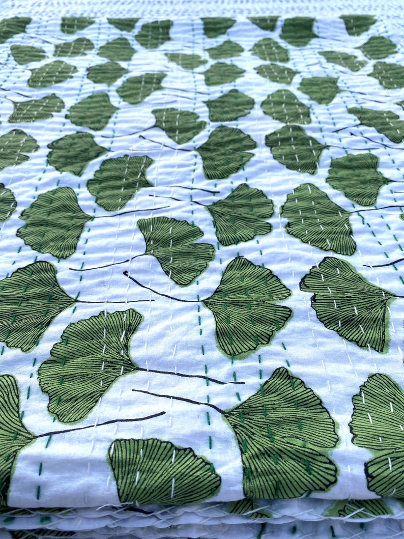May include: A white cotton kantha quilt with a green ginkgo leaf pattern. The quilt is hand-stitched and has a traditional Indian design.