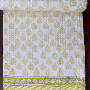 May include: A white cotton quilt with a yellow leaf pattern. The quilt has a yellow and white border with a geometric design.