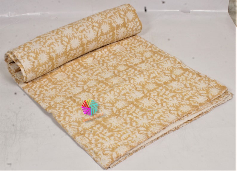 May include: A folded and rolled textile with a cream and mustard yellow floral design. The fabric is likely cotton or similar, suitable for bedding or home decor. The pattern repeats across the surface.
