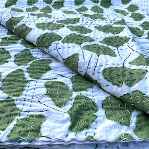 May include: White cotton kantha quilt with a green ginkgo leaf pattern. The quilt is folded in half and the leaves are stitched in a repeating pattern.
