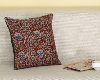 May include: A red, brown, and blue floral patterned throw pillow with a black border. The pillow is sitting on a white couch.