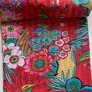 May include: Red kantha quilt with a floral pattern. The quilt features a variety of flowers in shades of pink, blue, green, and yellow. The quilt is made of cotton and is hand-stitched.