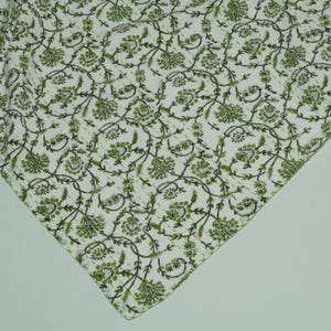 Green floral block print Kantha quilt rolled and unrolled on a white background, soft cotton hand-stitched blanket.