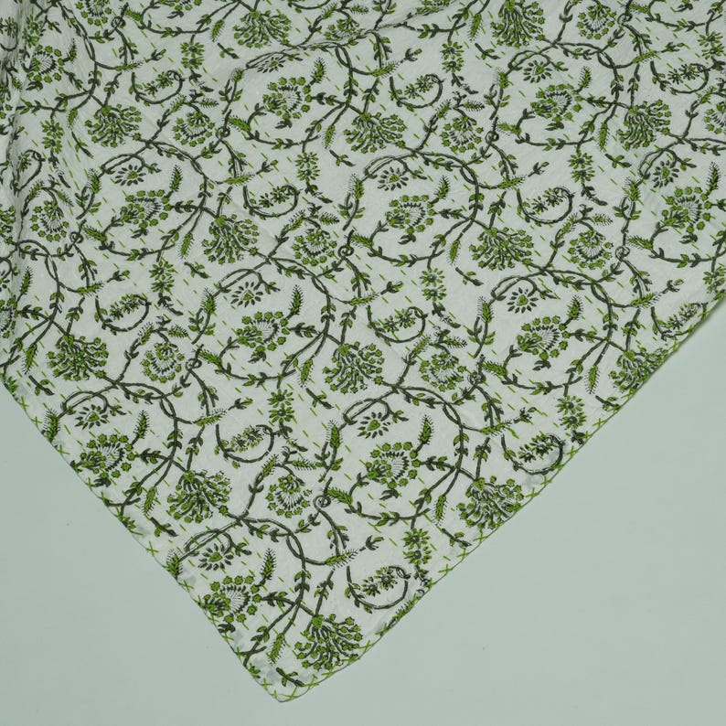 Green floral block print Kantha quilt rolled and unrolled on a white background, soft cotton hand-stitched blanket.