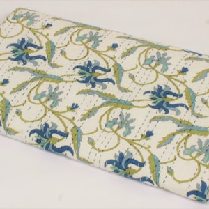 May include: A folded rectangular cotton quilt featuring an off-white base color with a repeating floral pattern in shades of dark blue, light blue, and olive green. The fabric displays visible running stitch details throughout the entire surface.