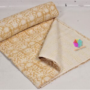 May include: A rolled-up, mustard-yellow and cream-coloured quilt with a floral pattern. The quilt is partially unfolded, revealing a cream-coloured underside with stitched lines. The quilt is made of soft fabric.