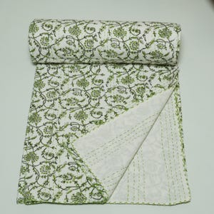 Green floral block print Kantha quilt rolled and unrolled on a white background, soft cotton hand-stitched blanket.