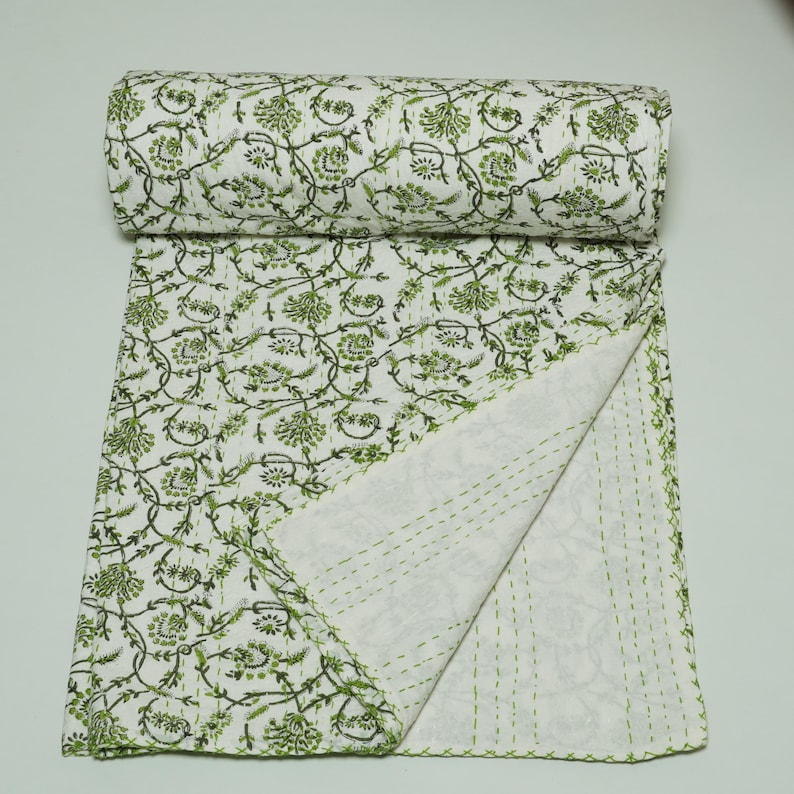 Green floral block print Kantha quilt rolled and unrolled on a white background, soft cotton hand-stitched blanket.