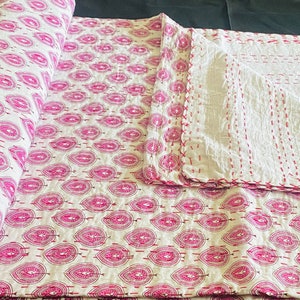 May include: A rolled-up white and pink quilt with a repeating leaf pattern. The quilt is hand-stitched with pink thread, and a portion is unfolded, revealing the reverse side with vertical stitching. The overall theme is home decor.