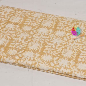 May include: Folded fabric with a cream and mustard yellow floral pattern. The design features stylized flowers and leaves. The fabric appears to be cotton or a similar natural fibre, suitable for quilting or crafting projects.