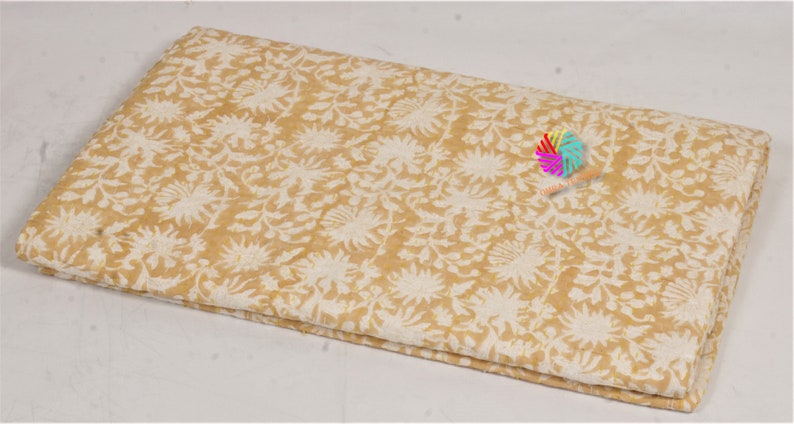 May include: Folded fabric with a cream and mustard yellow floral pattern. The design features stylized flowers and leaves. The fabric appears to be cotton or a similar natural fibre, suitable for quilting or crafting projects.