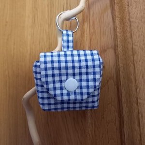 Peut inclure: Une petite pochette carrée avec un motif à carreaux vichy bleu et blanc. La pochette possède une boucle en tissu sur le dessus fixée à un anneau fendu en métal argenté. Un bouton-pression en plastique blanc ferme le rabat avant de l'objet.