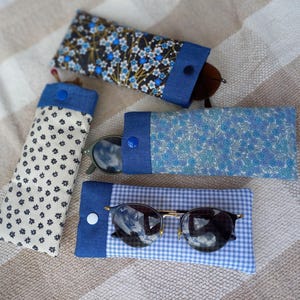 Peut inclure: Quatre étuis à lunettes rectangulaires en tissu avec fermetures à pression. Un étui est crème à fleurs noires, un bleu foncé à motifs floraux bleus, un bleu clair floral et un à carreaux vichy bleu et blanc avec des lunettes de soleil noires.