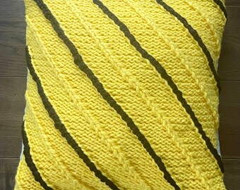 Può includere: Cuscino di maglia gialla con strisce diagonali nere. Il cuscino è realizzato con un motivo a treccia.