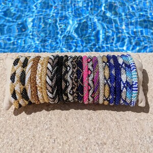 May include: A stack of colourful beaded bracelets in various patterns, including animal print, geometric, and stripes. The bracelets are arranged on a light brown surface.