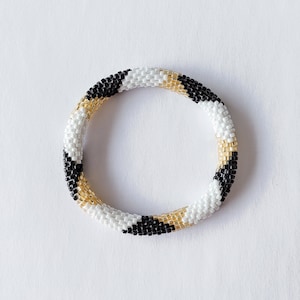 May include: A black, white and gold beaded bracelet with a geometric pattern.