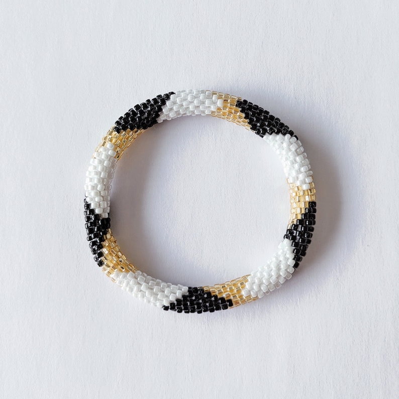 May include: A black, white and gold beaded bracelet with a geometric pattern.
