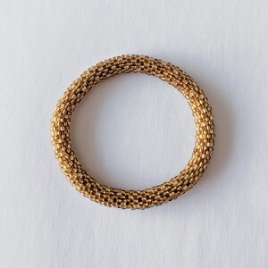 May include: A gold beaded bracelet with a round shape. The bracelet is made of small, square beads that are woven together.