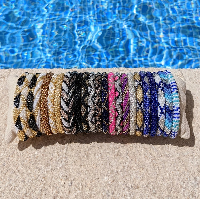 May include: A stack of colourful beaded bracelets in various patterns, including animal print, geometric, and stripes. The bracelets are arranged on a light brown surface.
