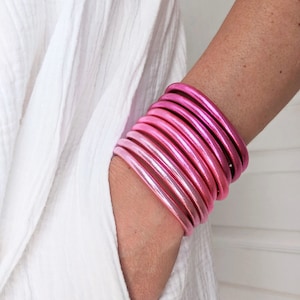 Może przedstawiać: Stos różowych bransoletek bangle z gradientem koloru od jasnoróżowego do ciemnoróżowego.