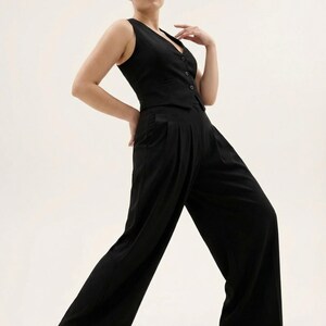 May include: A sleeveless black vest with a V-neck and button closure paired with wide-leg black trousers. The outfit is made of a smooth fabric and is suitable for various occasions. The model is posing on a white background.