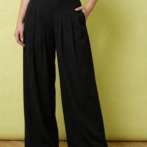 May include: Black high-waisted wide-leg trousers featuring front pleats and side pockets, paired with a matching black button-up vest top. The trousers have a loose, flowing silhouette that extends to the floor, creating a structured look.