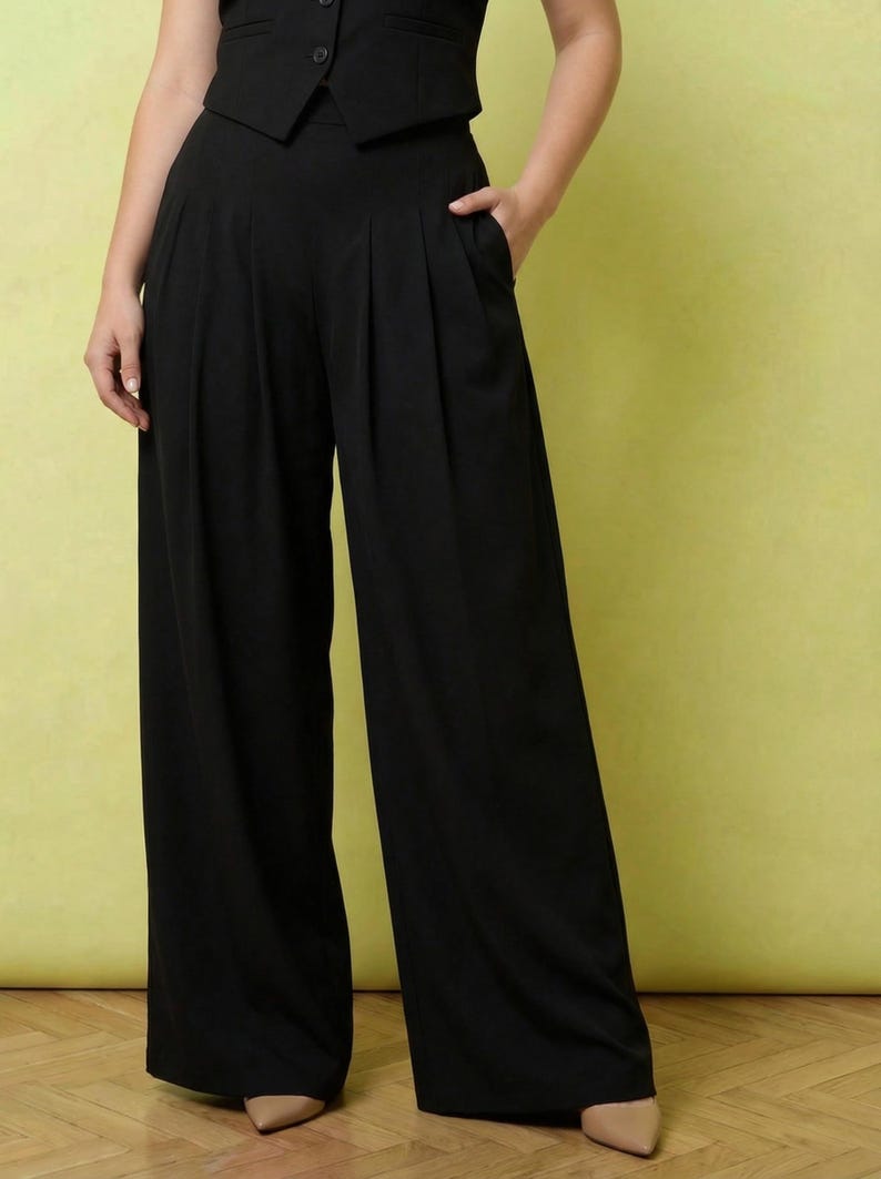 May include: Black high-waisted wide-leg trousers featuring front pleats and side pockets, paired with a matching black button-up vest top. The trousers have a loose, flowing silhouette that extends to the floor, creating a structured look.