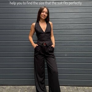 A woman in a black jumpsuit stands in front of a gray wall, smiling and posing for the camera.