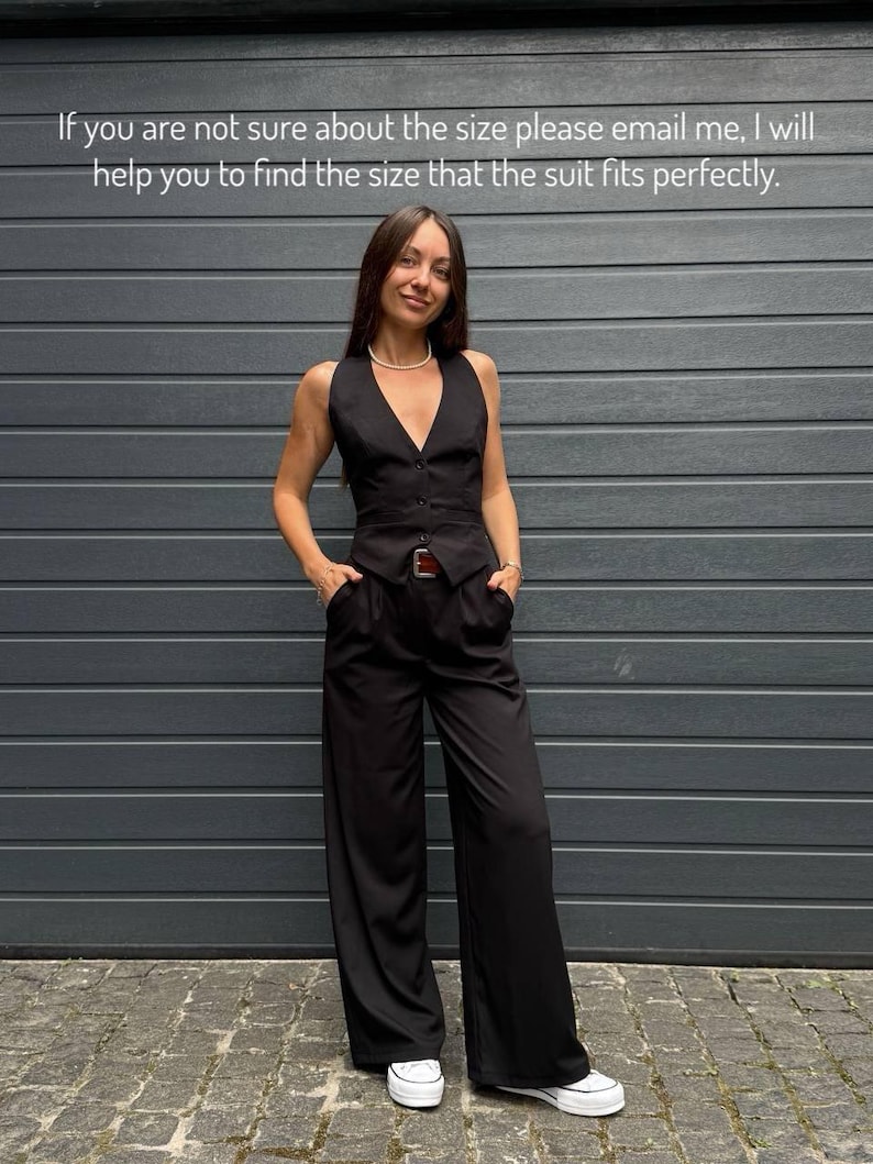 A woman in a black jumpsuit stands in front of a gray wall, smiling and posing for the camera.