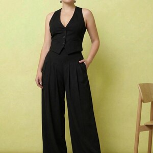 May include: A black sleeveless vest with a V-neckline and three front buttons paired with matching high-waisted wide-leg trousers featuring front pleats and side pockets. The ensemble is solid black and worn with pointed-toe beige heels.