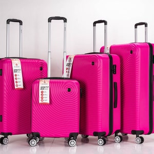 May include: Set of four pink suitcases with black handles and wheels. The suitcases have a circular pattern and the text "Spritz Air" is visible on the largest suitcase.