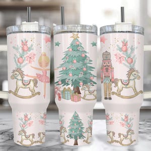 Op de afbeelding: Een witte beker met een handvat, met een kerstthema. Het ontwerp omvat een kerstboom, een ballerina, een notenkraker en schommelpaarden. De beker heeft een rietje en een inhoud van ongeveer 887 ml.