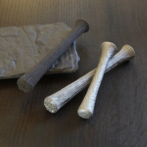 May include: Three decorative wooden sticks, two are silver and one is brown. The sticks are on a dark wood surface.