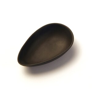 May include: A black ceramic dish shaped like a teardrop. The dish is smooth and glossy.