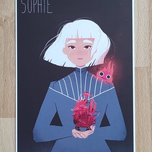 May include: A digital illustration of a woman with white hair holding a red flying machine in her hands. The woman is wearing a blue dress with white stripes. The background is black with the word "SOPHIE" at the top.
