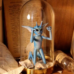 May include: A blue figurine of a winged creature, displayed under a glass dome with a gold base. The figurine is in a dynamic pose. The background features aged papers and a glass bottle.