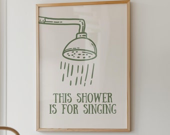 May include: A framed print with a green illustration of a shower head and the text "This shower is for singing". The print is hanging on a white wall above a wooden cabinet with a yellow lamp, a stereo system, and a keyboard.